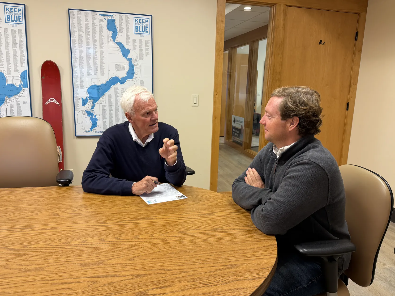 Kirk Stauss talking with a client at a conference table in the Stauss Realty office in Okoboji, Iowa