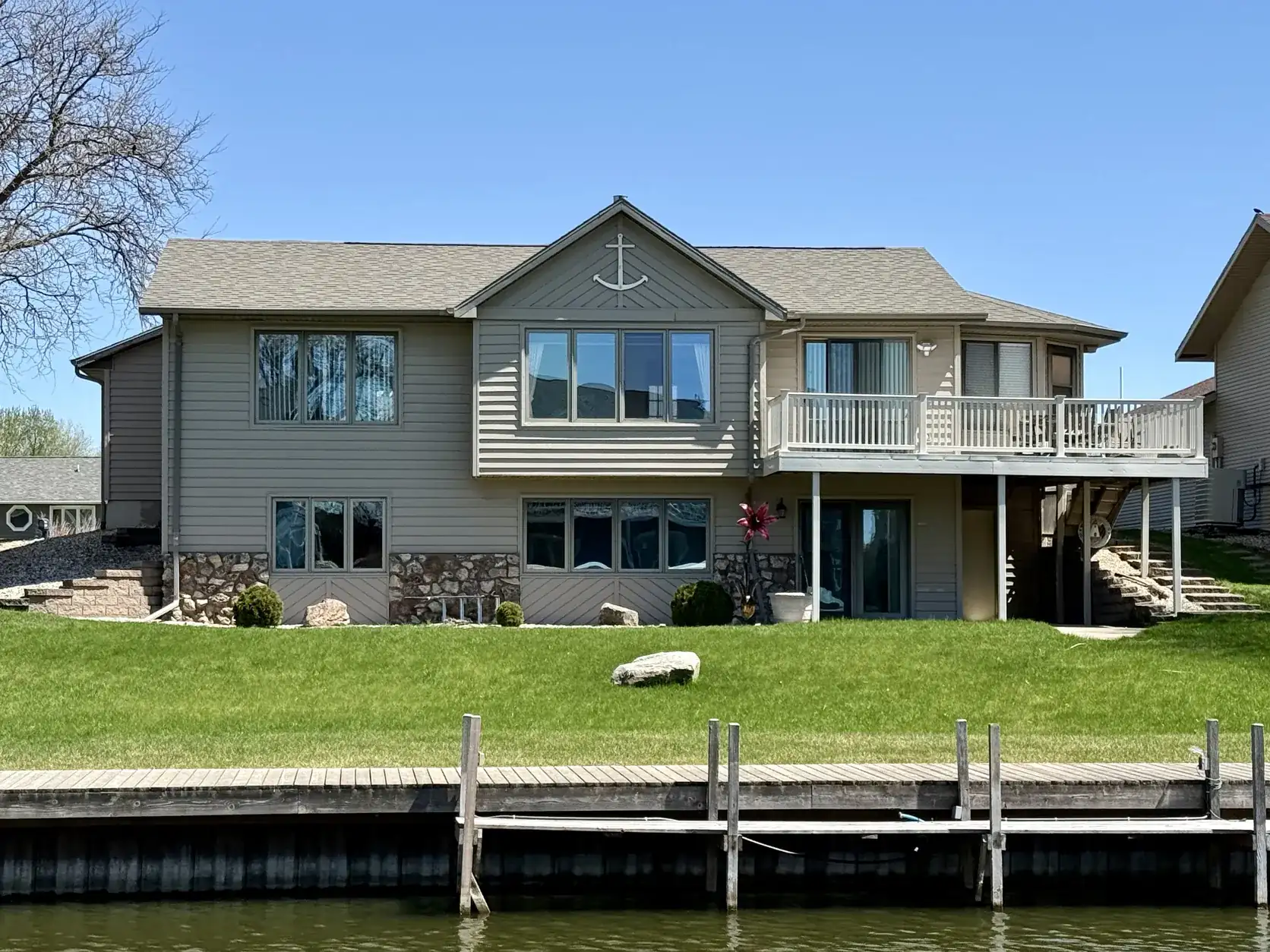Listing photo of a two-story home with a lawn, seawall and dock on the water in Spirit Lake, Iowa